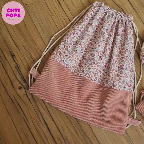Vidéo présentant le sac à dos format pochon pour enfant motif liberty. On peut y voir le sac sans rabat, la version avec un rabat en velours côtelé rose et la pochette à goûter assortie.