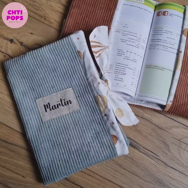 Vidéo présentant le protège carnet de santé en velours côtelé par Chtipops Créations. Ce protège carnet de santé se ferme grâce à un ruban en tissu imprimé à motif et est personnalisable avec le prénom de l'enfant qui sera floqué sur une petite étiquette en tissu.