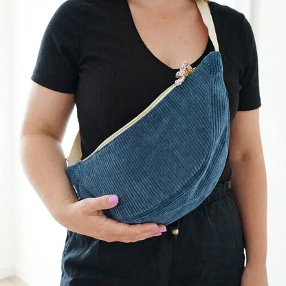 Sac banane bleu foncé en velours côtelé porté en travers, zip clair et nœud fleuri sur la tirette