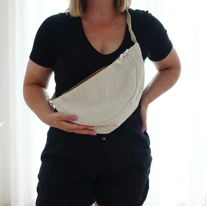 Sac banane écru en velours côtelé porté en travers du buste, zip cuivré et sangle assortie