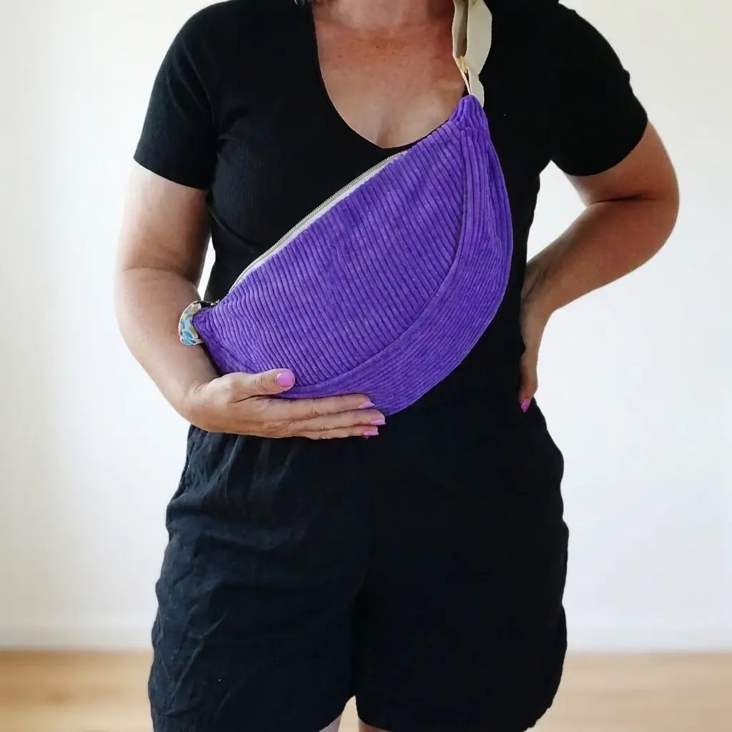 Sac banane violet en velours côtelé porté en bandoulière, tirette ornée d'un nœud en tissu