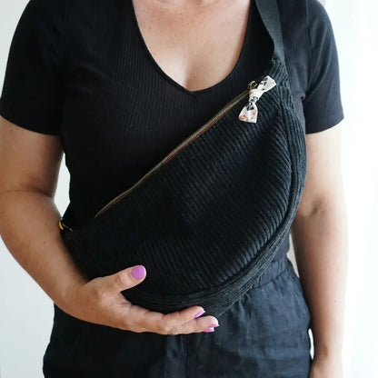 Sac banane noir en velours côtelé porté en bandoulière, sangle noire et nœud motif léopard sur le zip