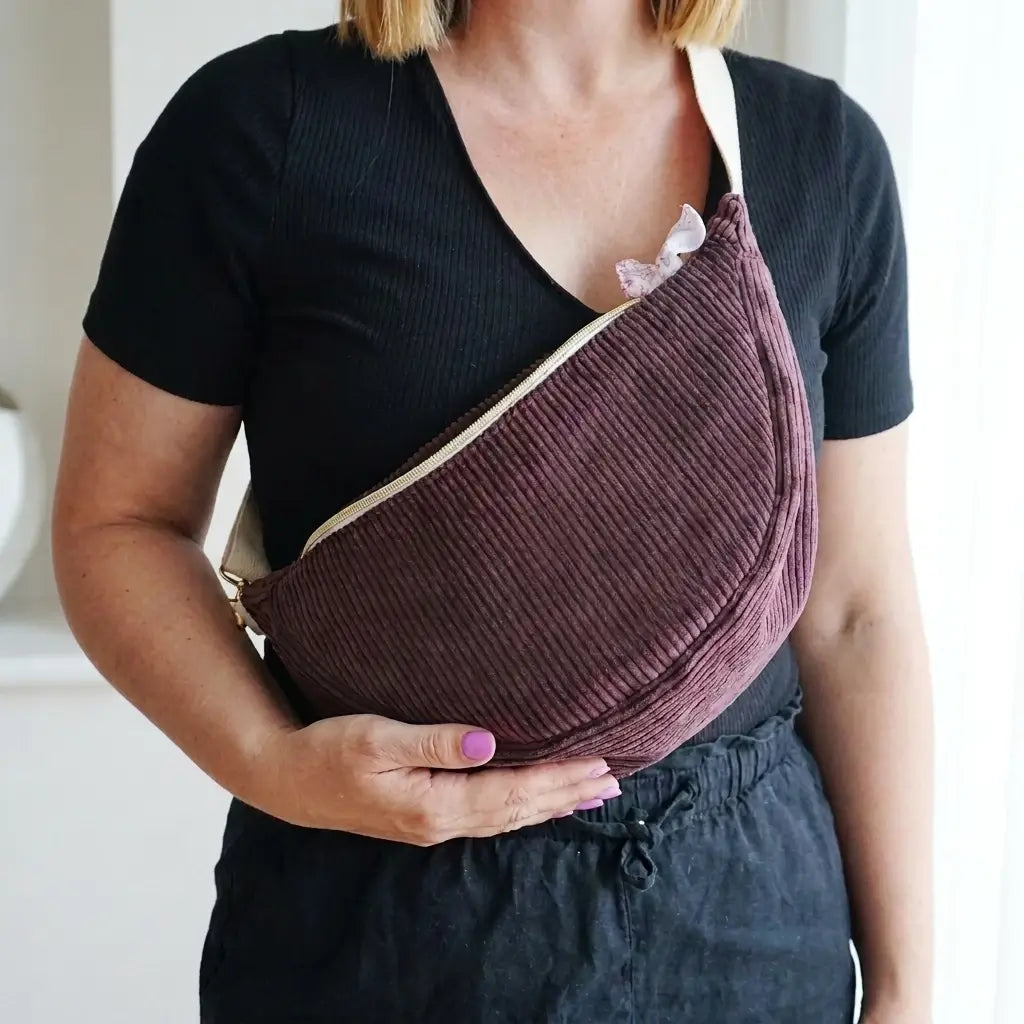 Sac banane prune en velours côtelé de forme demi-lune, porté en travers avec sangle écrue