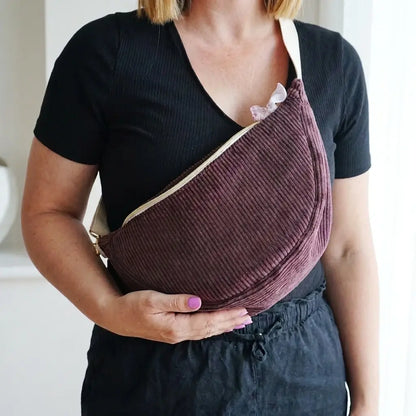 Sac banane prune en velours côtelé de forme demi-lune, porté en travers avec sangle écrue