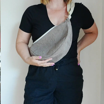 Sac banane taupe en velours côtelé porté en travers du buste, sangle écrue et zip blanc