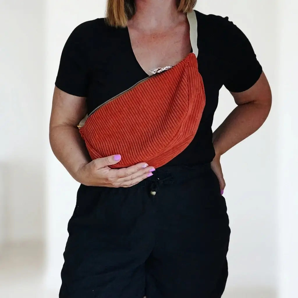Sac banane terracotta en velours côtelé porté en bandoulière sur un pantalon noir