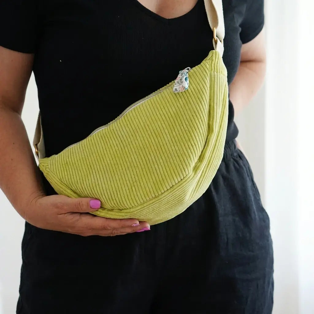 Sac banane vert anis en velours côtelé vu de près, porté avec sangle beige et tirette fleurie