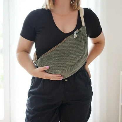 Sac banane vert en velours côtelé porté en travers, nœud fleuri accroché au curseur du zip
