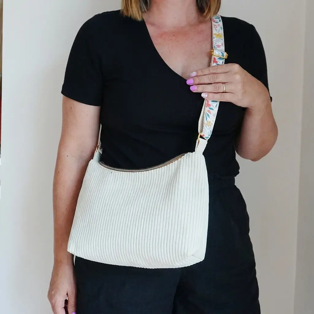 Sac bandoulière écru en velours côtelé porté en travers, large sangle fleurie et boucle dorée