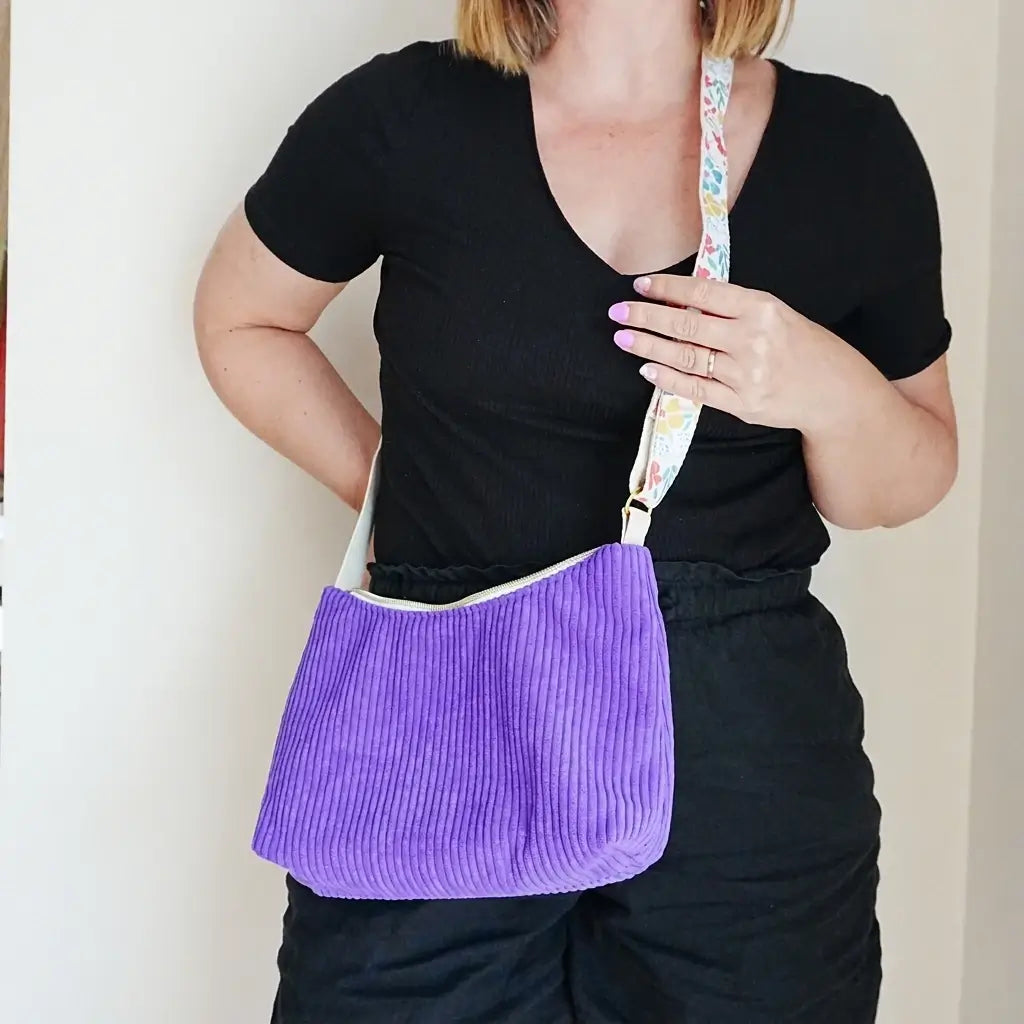 Sac bandoulière violet en velours côtelé porté en travers, sangle à fleurs multicolores