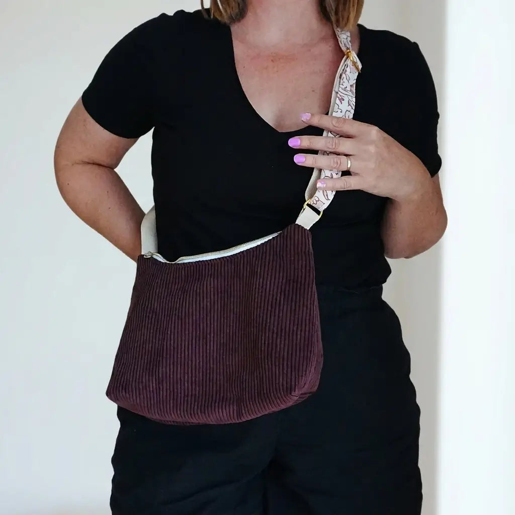 Sac bandoulière prune en velours côtelé porté à la hanche, sangle imprimée et zip clair