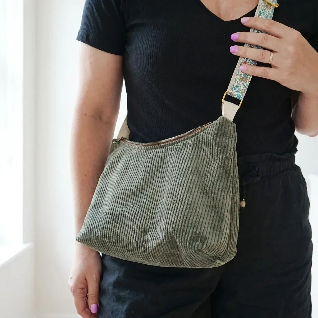 Sac bandoulière vert en velours côtelé vu de près, sangle fleurie tenue à la main