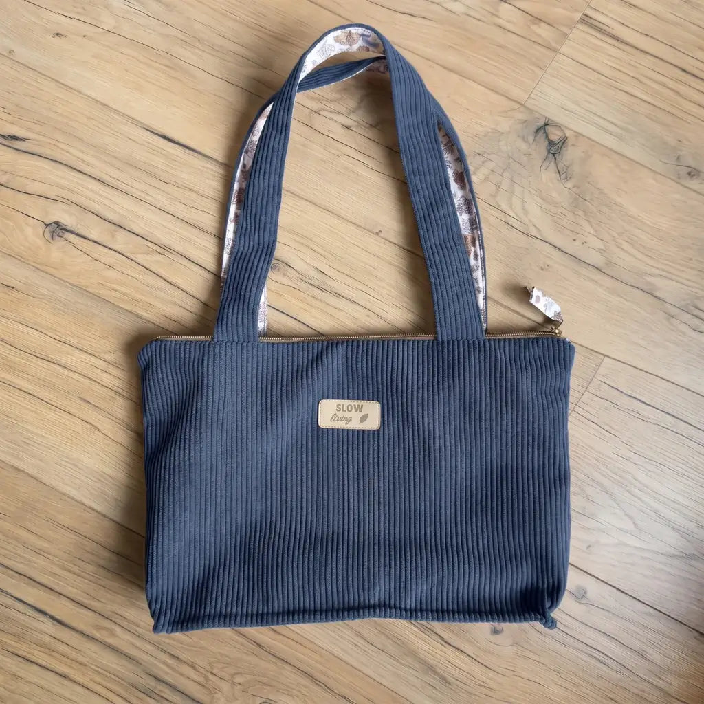 Sac cabas bleu foncé en velours côtelé posé à plat, anses doublées de tissu fleuri et fermeture zippée