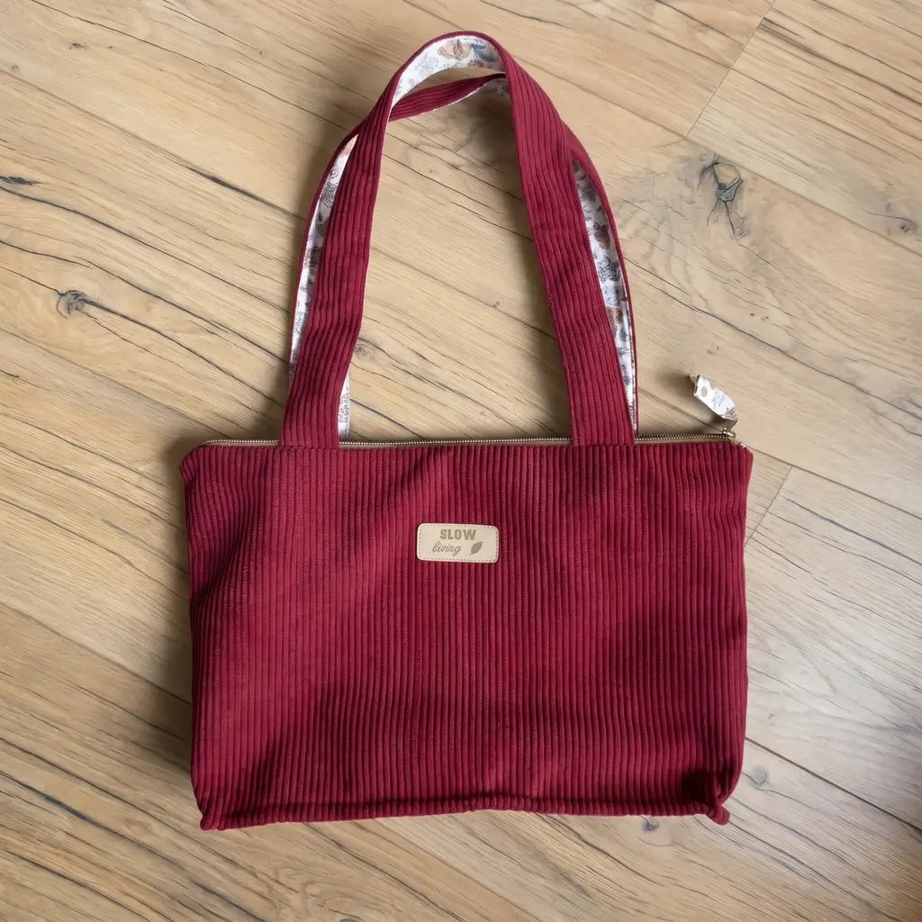Sac cabas rouge bordeaux en velours côtelé posé sur un parquet, anses larges et fermeture zippée