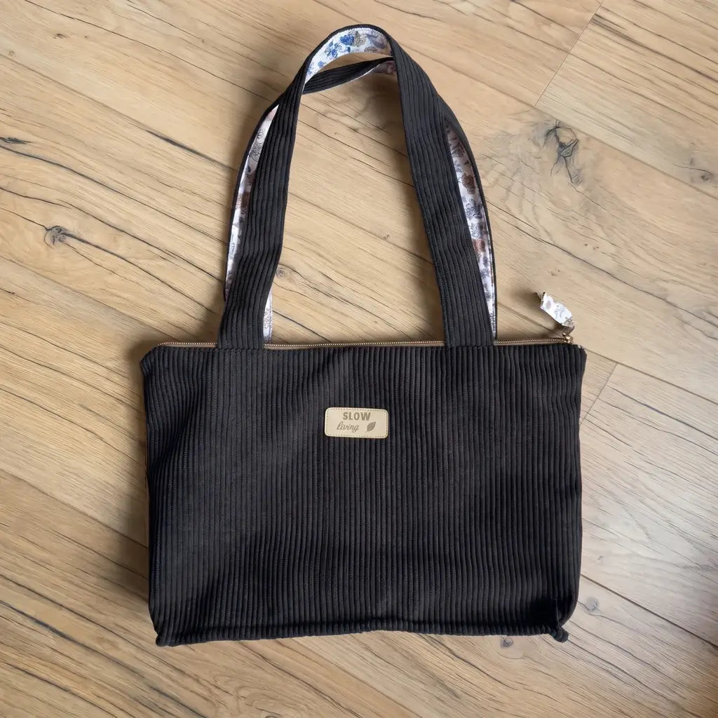 Sac cabas noir en velours côtelé posé à plat, intérieur des anses à motif fleuri et zip doré