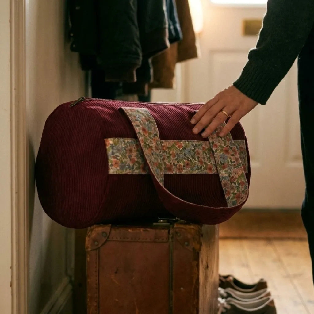 sac polochon velours côtelé prune posé sur valise dans une entrée maison
