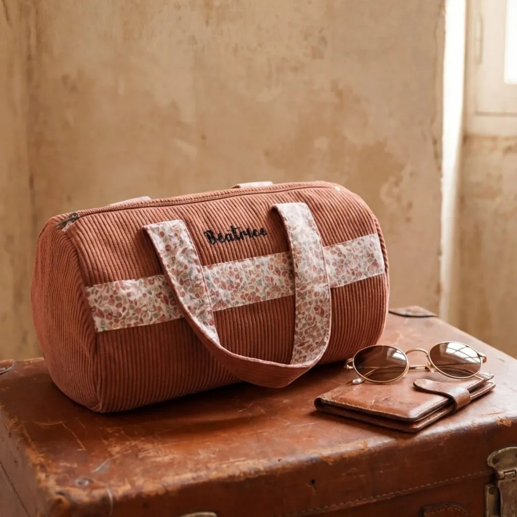 sac polochon velours côtelé rose posé sur valise en cuir style voyage