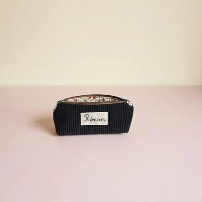 Trousse d'école noire en velours côtelé, doublure claire à taches brunes et étiquette prénom sur la face