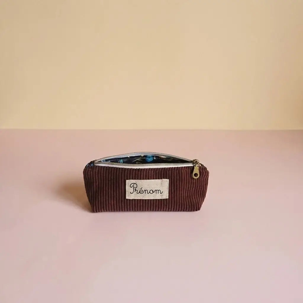 Trousse d'école prune en velours côtelé, doublure sombre à motif bleu et étiquette prénom au centre