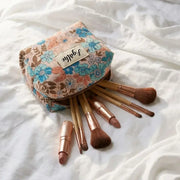 trousse maquillage fleurie en tissu motif hibiscus avec pinceaux sur lit blanc