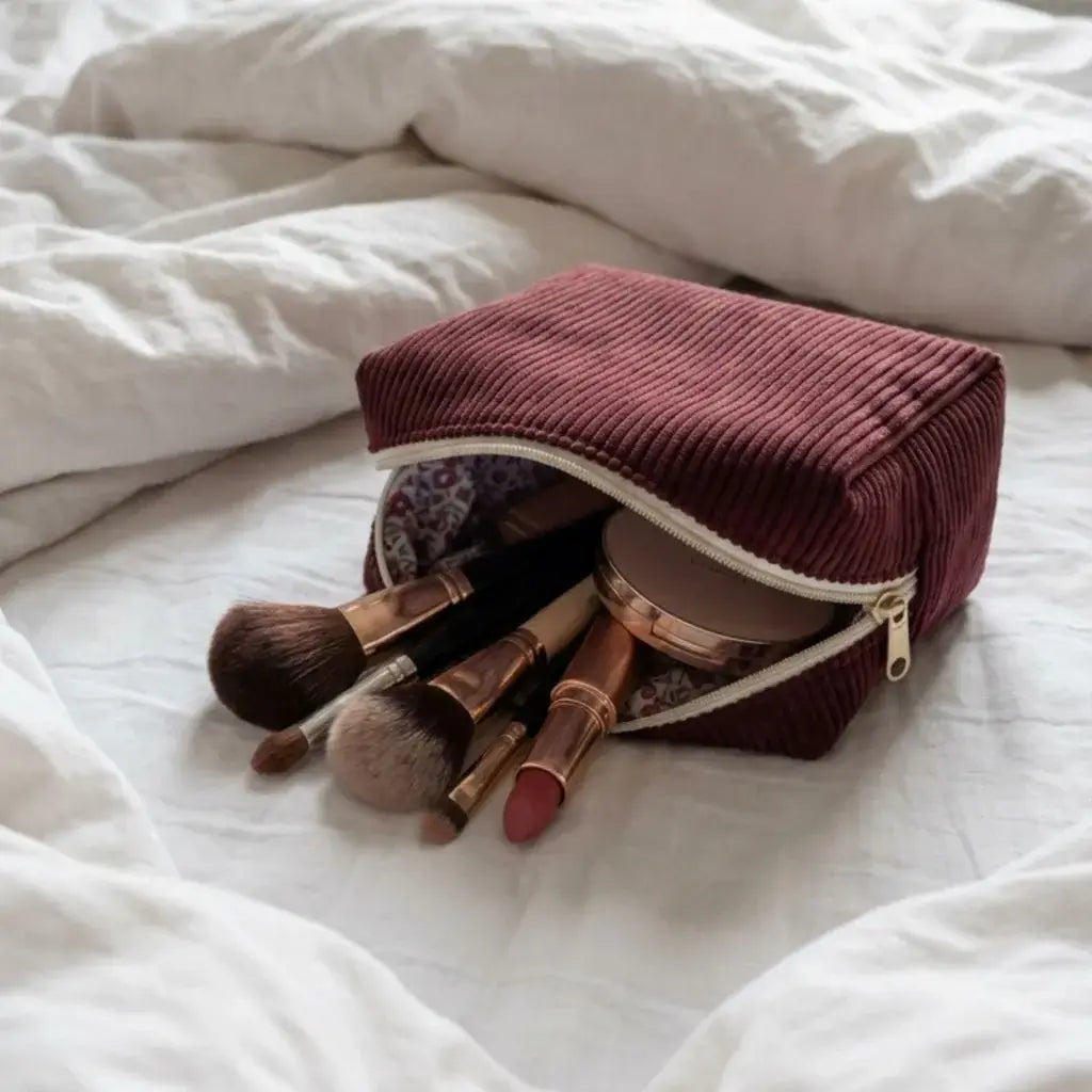 trousse maquillage velours côtelé prune avec accessoires beauté sur lit