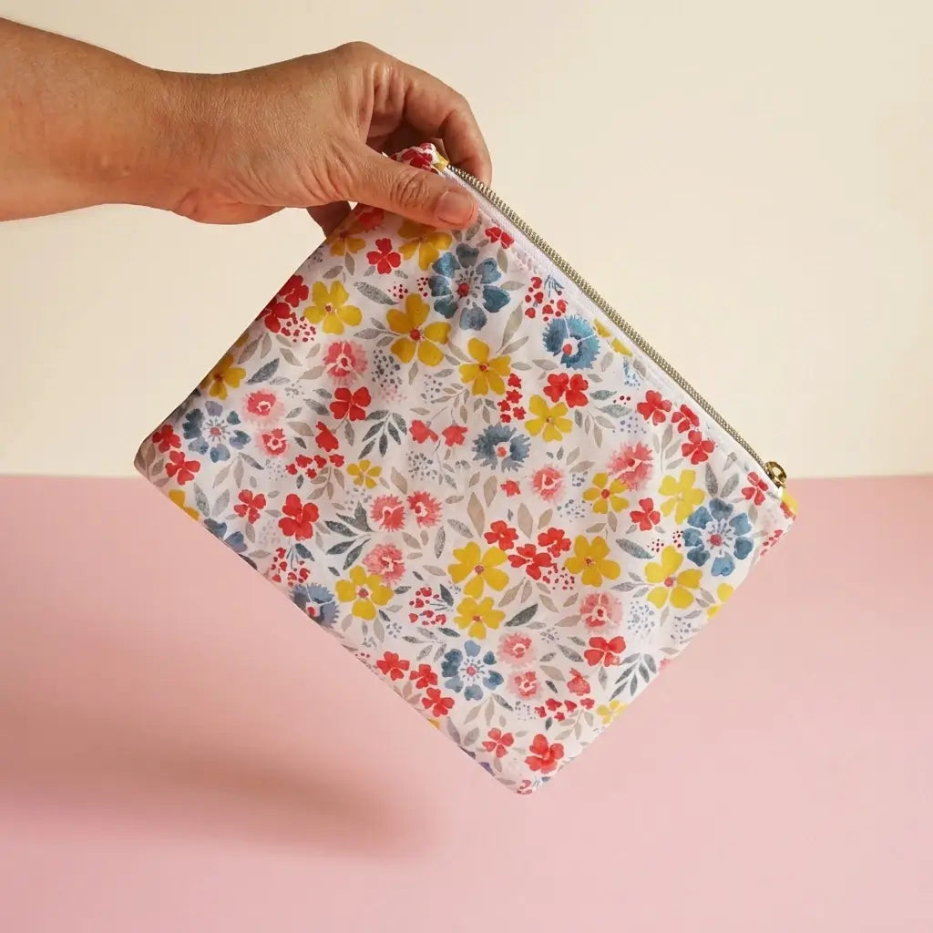 Trousse plate zippée à fleurs jaunes, rouges et bleues tenue à la main pour montrer sa taille