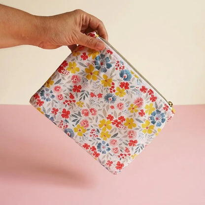 Trousse plate zippée à fleurs jaunes, rouges et bleues tenue à la main pour montrer sa taille