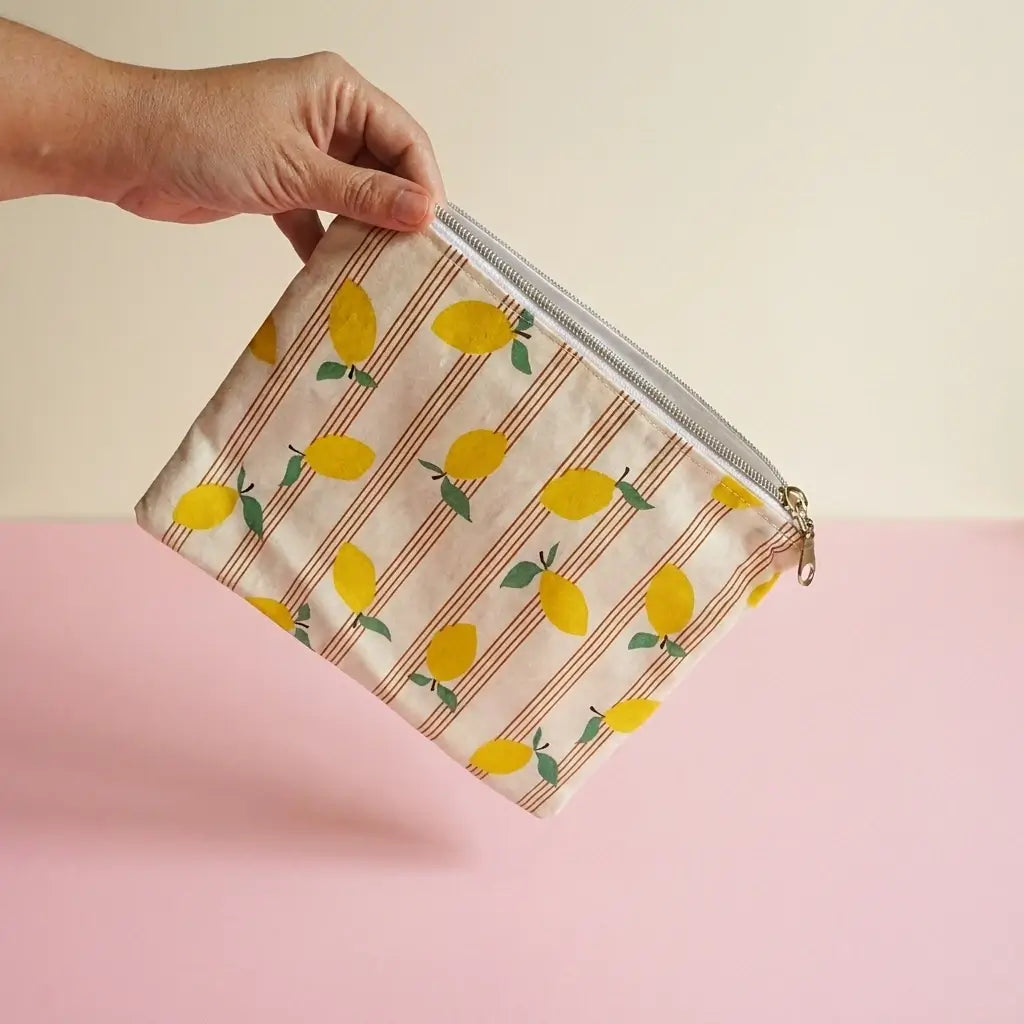 Trousse plate zippée à motif citrons et rayures tenue à la main, fermeture éclair visible