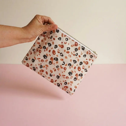 Trousse plate zippée à motif léopard écru, brun et noir tenue à la main par le zip
