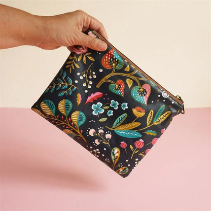 Pochette plate zippée à motif floral coloré sur fond noir, tenue à la main par le zip