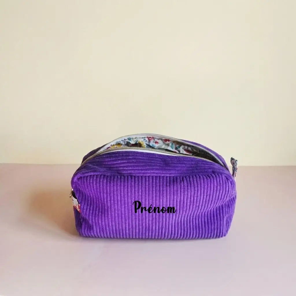 Trousse de toilette violette en velours côtelé, doublure fleurie multicolore visible et prénom sur le devant