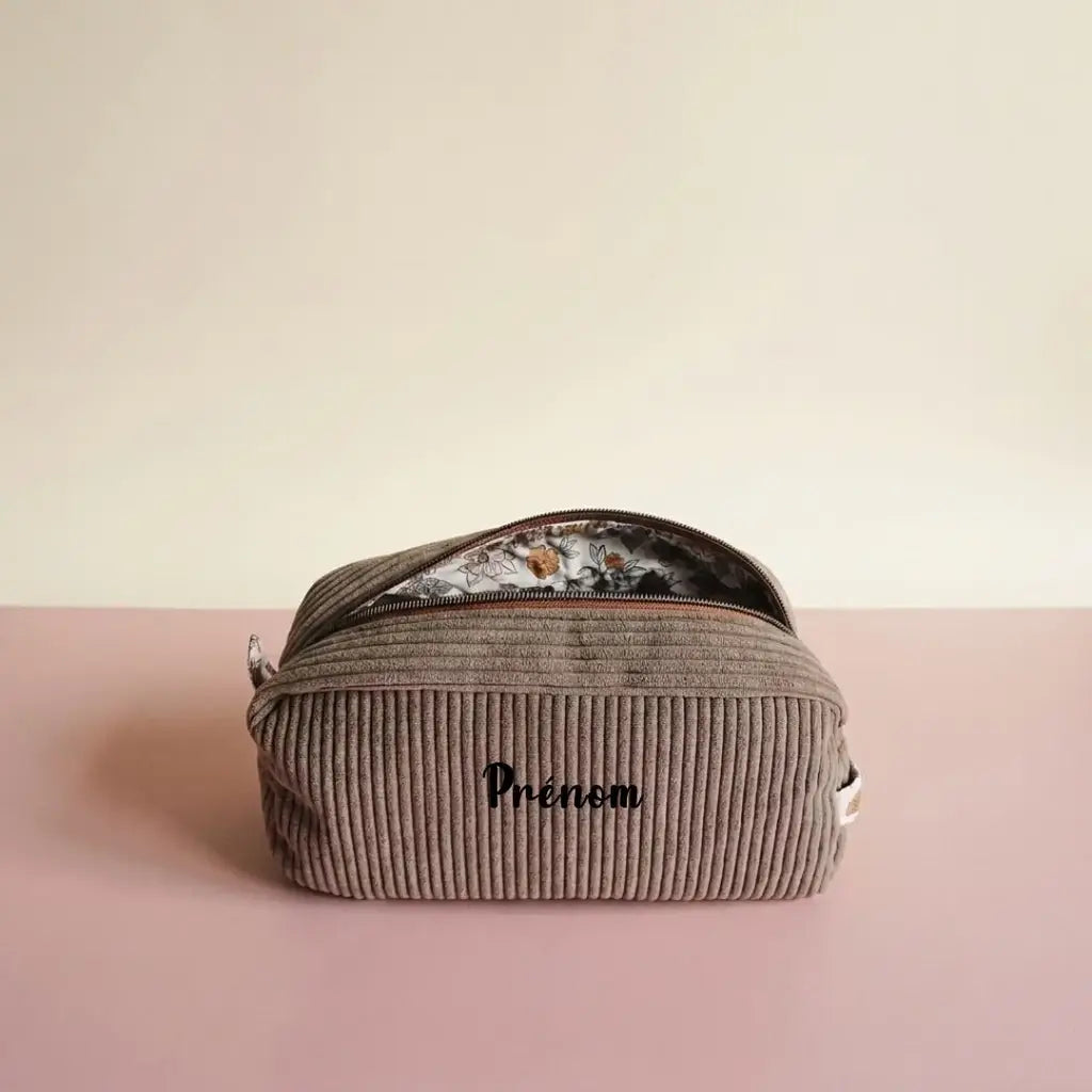Trousse de toilette taupe en velours côtelé, zip marron entrouvert sur doublure à fleurs ocre, prénom devant