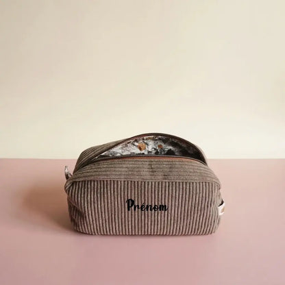 Trousse de toilette taupe en velours côtelé, zip marron entrouvert sur doublure à fleurs ocre, prénom devant